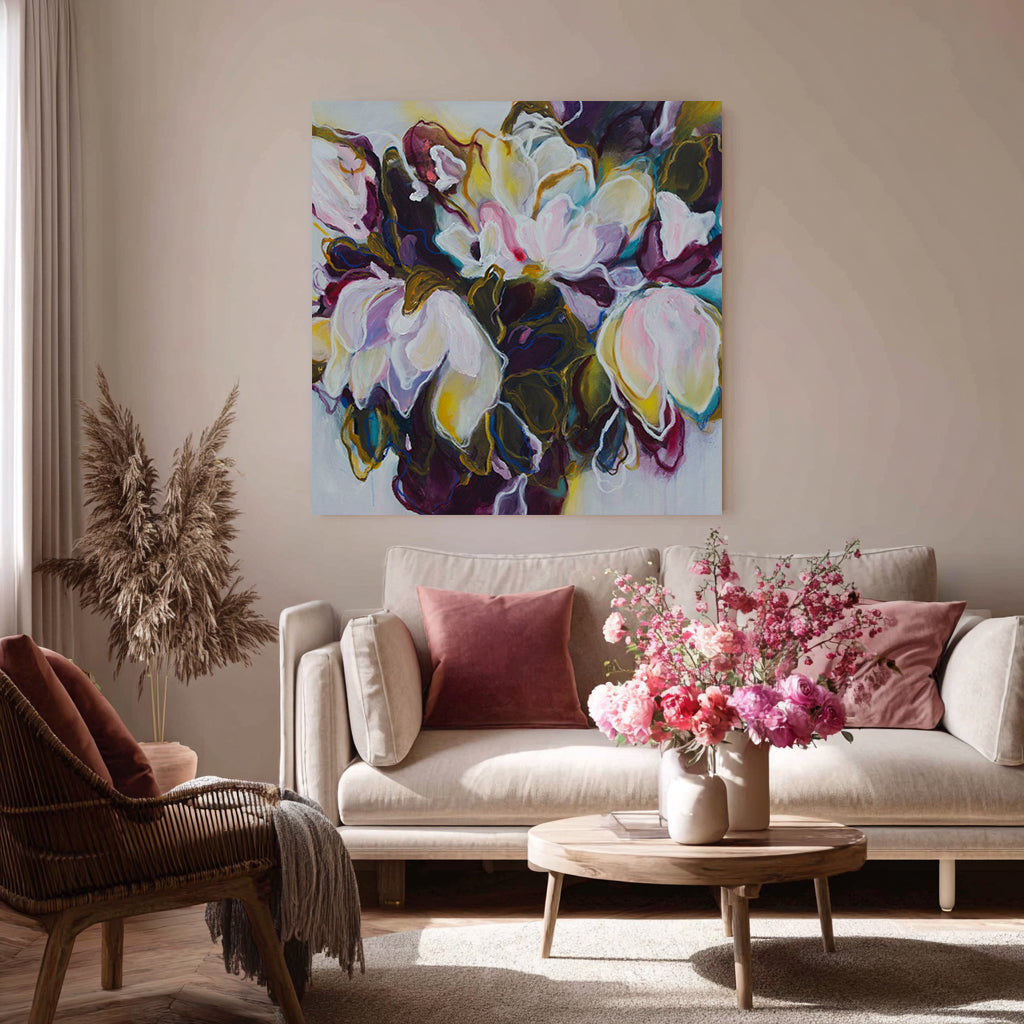Living room with a floral painting on the wall, a beige sofa with pink cushions, and a wooden coffee table with flowers.