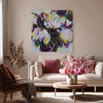 Living room with a floral painting on the wall, a beige sofa with pink cushions, and a wooden coffee table with flowers.