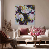 Living room with a floral painting on the wall, a beige sofa with pink cushions, and a wooden coffee table with flowers.