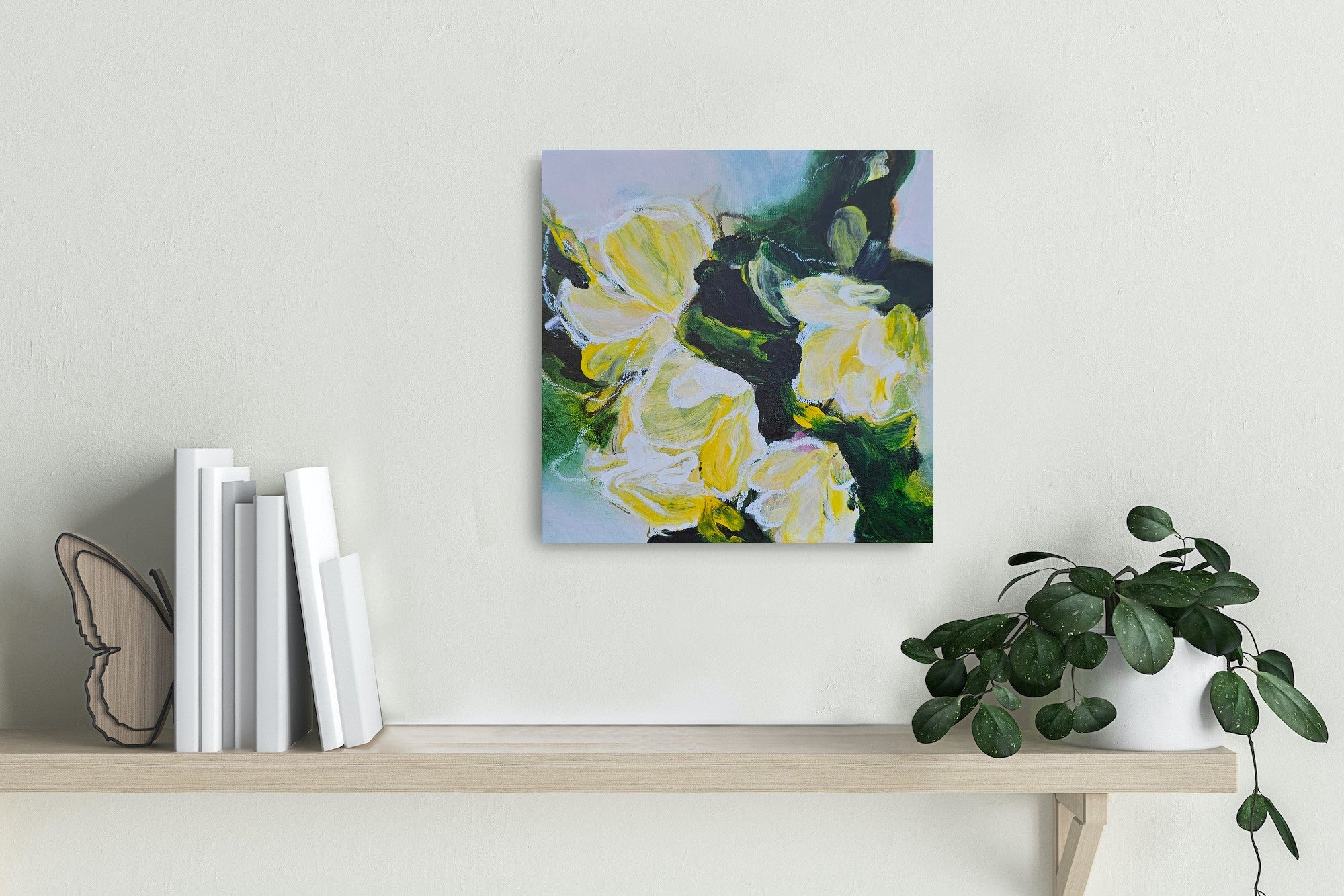 Framed floral painting on a shelf with books and a plant