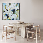 A large square 48 x 48” abstract, botanical original artwork done by the Canadian artist Mona in the colours of blues, beige, dark greens and white framed in a black frame on the wall in a kitchen
