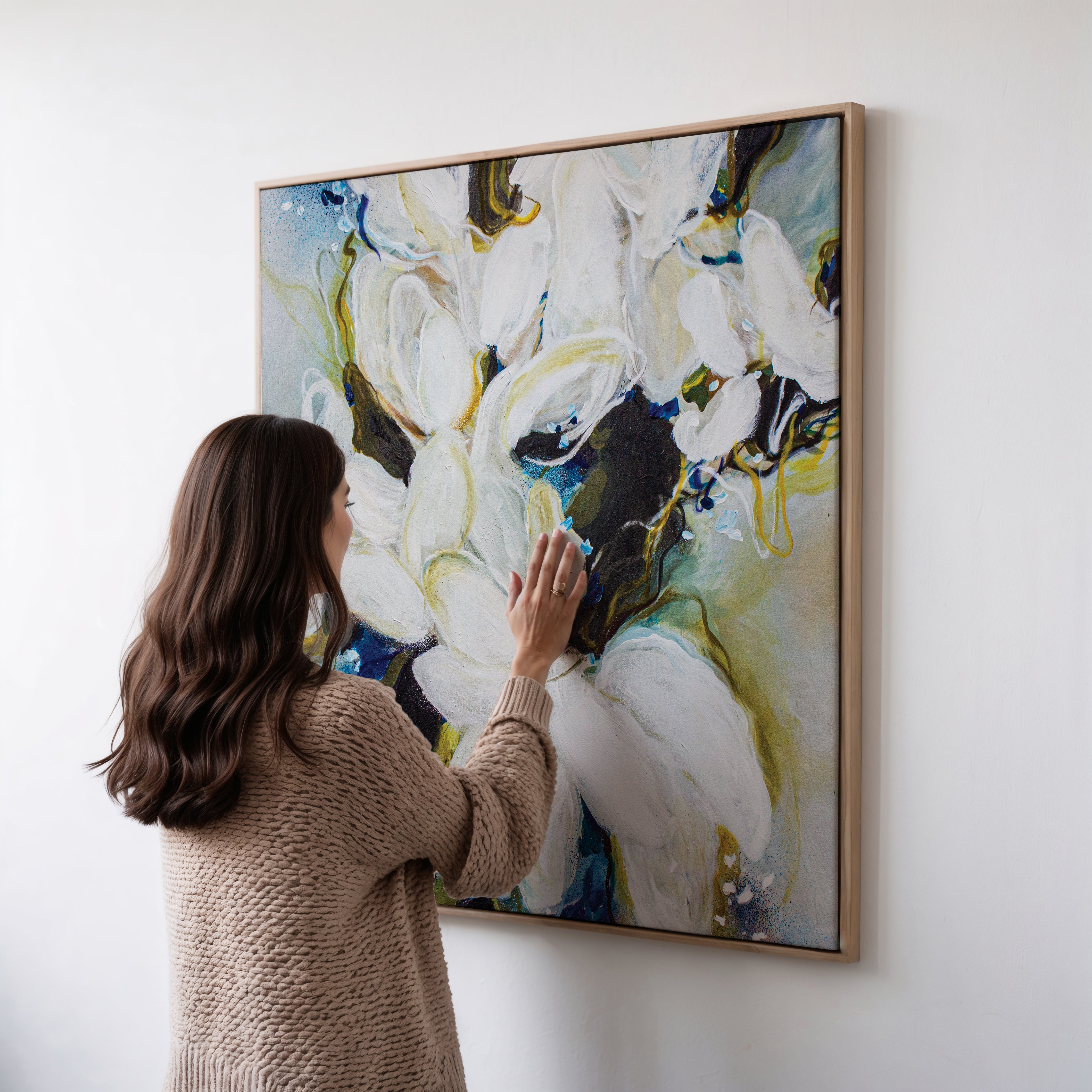 A large square original artwork done by the Canadian artist Mona in a floating frame hanged on a wall the colour of the paintings are blues, yellows dark greens, and lots of whites