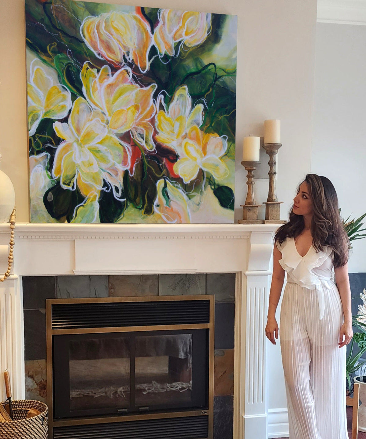 The artist standing in a room with a colorful floral painting above a fireplace.