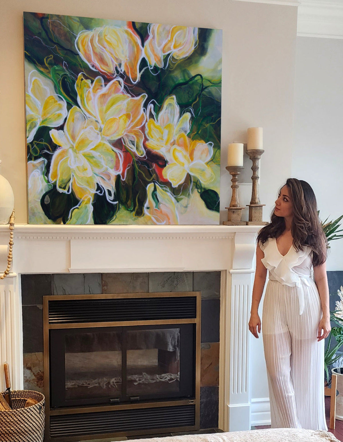 The artist standing in a room with a colorful floral painting above a fireplace.